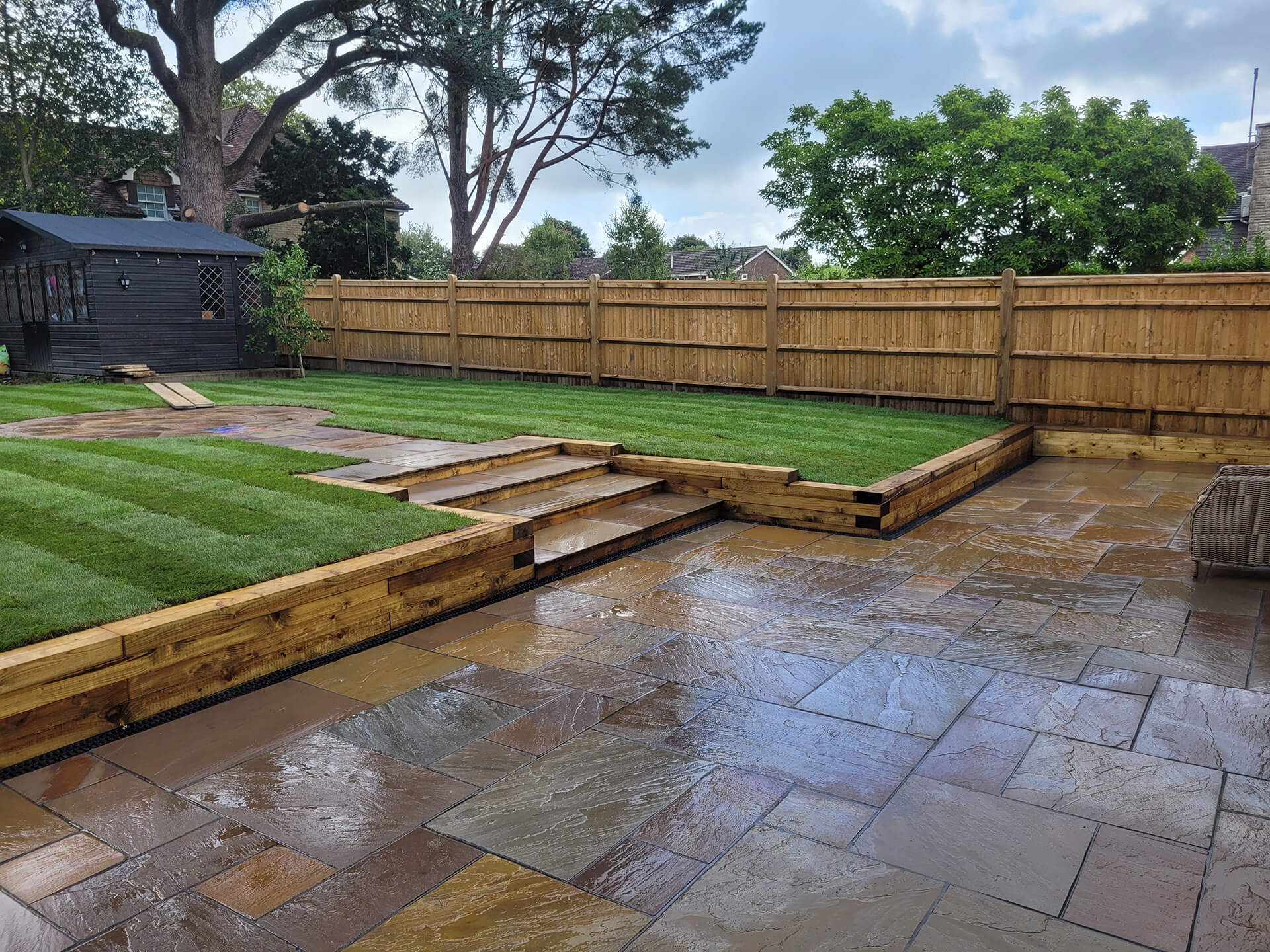 Patio and garden landscaping by Deerwood Construction in Crowborough East Sussex featuring terraces, lawn, and timber steps.